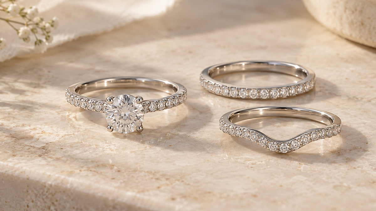 Diamond engagement ring displayed with straight and contoured wedding band options on a soft ivory stone surface.