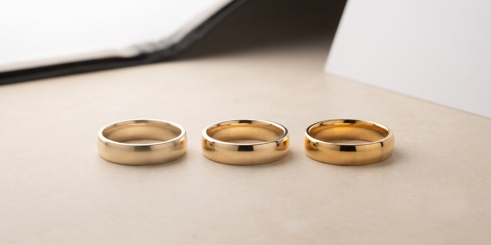 Three plain yellow-gold bands arranged from left to right, showing the progressively richer color of 10K, 14K, and 18K gold.
