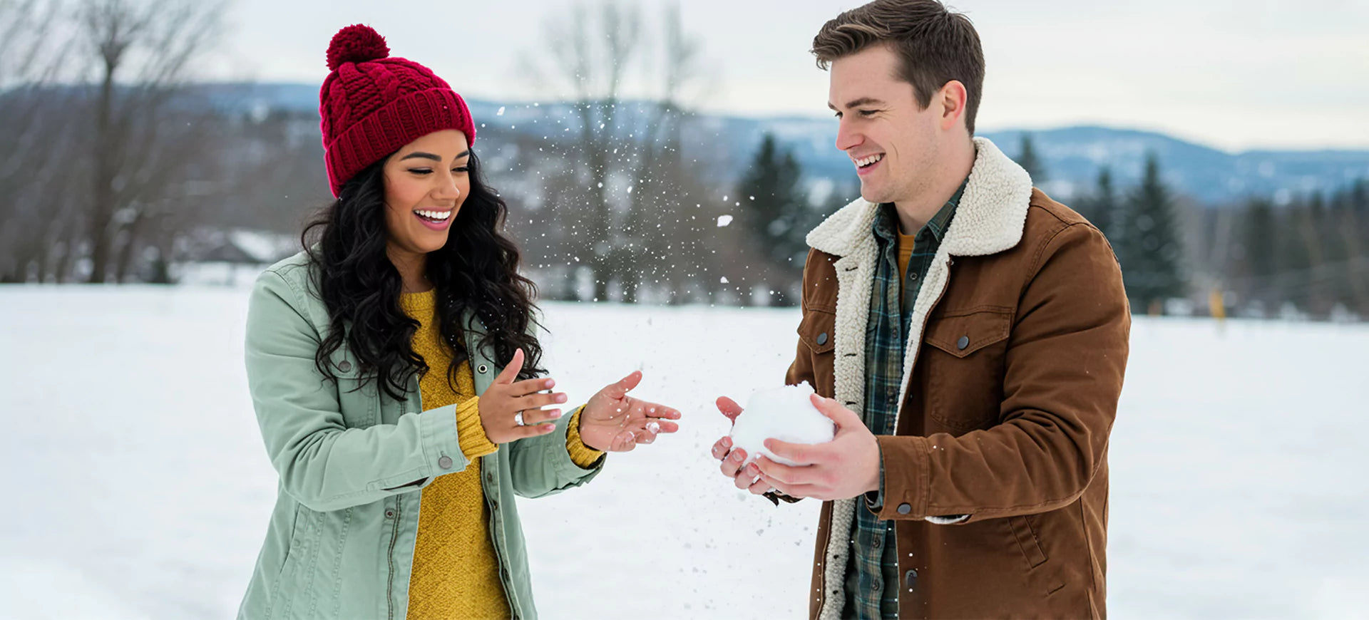  Joyful couple playing in the snow, with the woman’s sparkling engagement ring catching the light and adding elegance to the playful winter moment.